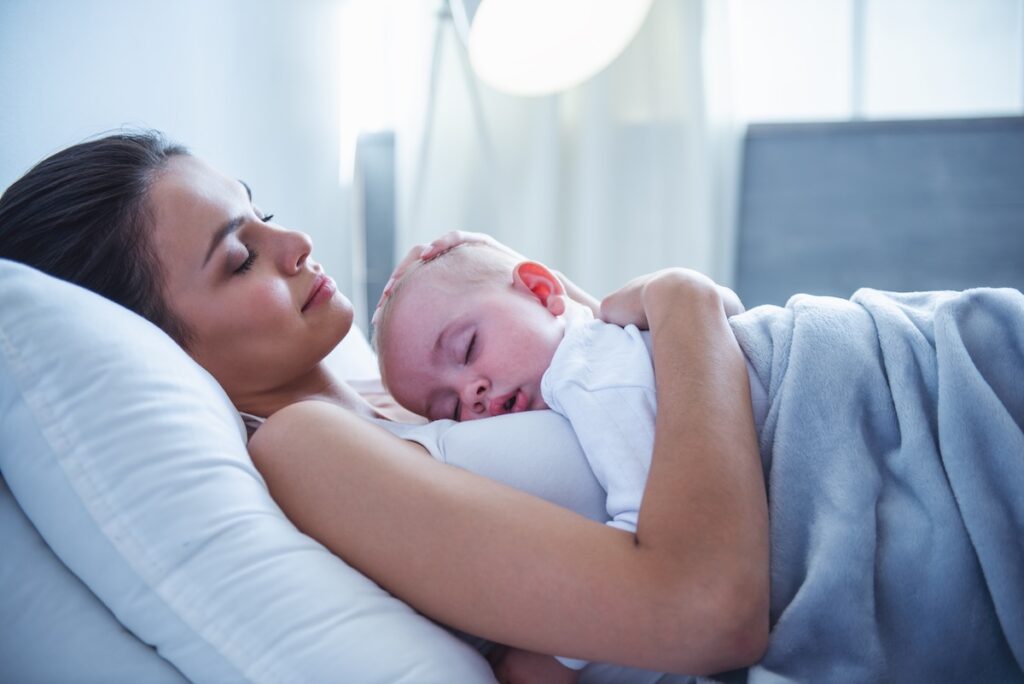 Mom and baby asleep together with baby resting on her chest in bed