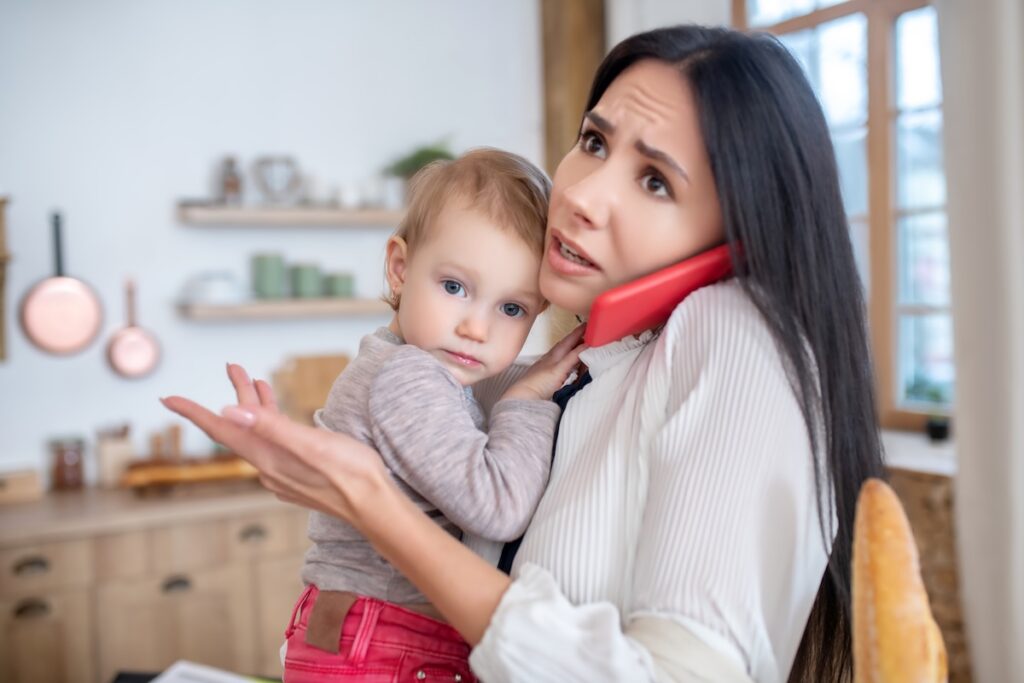 Mother holding her baby while looking confused during a phone call