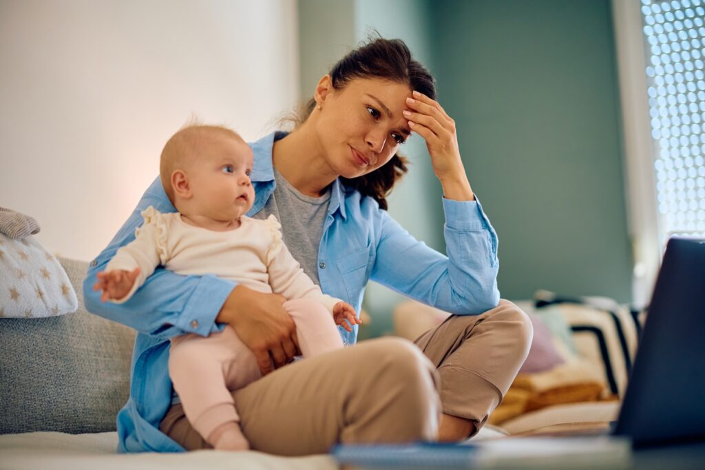 Mother doesn't know which advice to take. Looking stressed at computer holding baby.