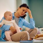 Mother doesn't know which advice to take. Looking stressed at computer holding baby.